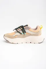 Zapatilla urbana de diseño chunky, con paneles combinados en tonos beige, arena y gris. Presenta cordones jaspeados en azul y amarillo, tirador trasero amarillo y suela de plataforma dentada en color crema.