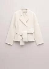 Chaqueta de mezcla de lana, poliéster y elastano color marfil, con solapas cruzadas, cuello alto y cinturón ajustable del mismo tejido. Cuenta con mangas largas y forro interior de viscosa.
