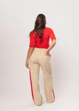 Pantalón beige de tiro alto con bolsillos delanteros y traseros, cierre frontal con cremallera y botón, y detalle de pespuntes rojos en los laterales.