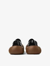 Mocasín de cuero vacuno color negro con diseño híbrido y suela voluminosa de aspecto amaderado.