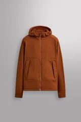 Chaqueta de hombre color marrón óxido con textura de pequeños cuadrados en relieve. Presenta cierre frontal de cremallera, capucha ajustable, bolsillos laterales con solapa y puños ajustables. El interior es de forro polar.