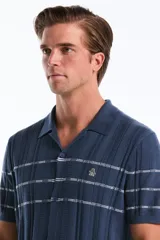 Polo cardigan azul de tejido de punto con rayas horizontales blancas en el pecho, cuello camisero y cierre frontal de botones.