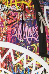 Mochila Sprayground con estampado de graffiti multicolor y diseño de boca de tiburón con dientes blancos. Cuenta con bolsillo frontal con cremallera, bolsillos laterales, bolsillo oculto con cremallera, compartimento para gafas de sol, acolchado ergonómico en la parte posterior, correas ajustables, cierres dorados, placa metálica con logo, compartimento para laptop y espalda ergonómica con malla.