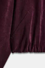 Cazadora bomber de Zara, de color bordó, con cuello de solapa, manga larga, bolsillos de vivo en el delantero y bajo elástico. Cuenta con cierre frontal de cremallera metálica.
