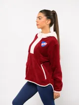Buzo de micropolar color bordó con capucha, cierre frontal parcial y detalles en color crema. Presenta el logo de Umbro y el escudo del Club Nacional de Football bordados en el frente.