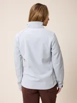 Campera softshell blanca con cierre frontal completo, cuello alto y bolsillos laterales. Presenta un bolsillo vertical con cierre en el pecho y el logo de la marca bordado.