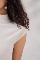 Top sin mangas, cuello tortuga, color blanco con acabado brillante o metálico. Tejido acanalado y ajustado al cuerpo.