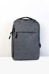 Mochila gris de poliéster con compartimento principal con cierre, bolsillo frontal con cierre, bolsillos laterales y asa superior.