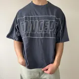 Remera gris oscuro de corte boxy y mangas cortas, con un gran estampado frontal en el pecho que dice "CONCEPT" en líneas blancas.