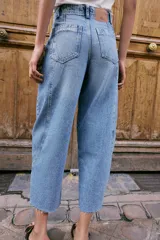 Jeans de tiro alto con corte barrel, pernera holgada que se estrecha hacia el tobillo y bajo deshilachado. Presenta costuras verticales decorativas en el frente y cierre frontal con cremallera y botón.