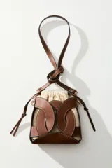 Cartera bombonera combinada de cuero sintético marrón con pespuntes blancos y bolsa interior de lona de mezcla de algodón y lino. Cuenta con diseño estructurado, cierre ajustable con cordón y correa bandolera extraíble con mosquetones metálicos dorados.