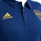 Chomba azul con cuello clásico y tapeta de botones. Presenta las tres tiras características de Adidas en los hombros y el logo de la marca bordado en dorado en el pecho. También incluye el escudo del club Boca Juniors bordado en el pecho.