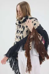 Ruana de punto triangular tejida en lambswool, con diseño geométrico en tonos tostado, blanco y negro, terminada con flecos en los bordes.