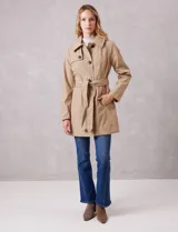Gabardina trench de tejido repelente al agua en color beige. Presenta cuello con solapa ancha, cierre frontal con botones en tono carey, capucha desmontable y lazo de ajuste en la cintura. Incluye bolsillos laterales tipo ojal y forro interno a tono.