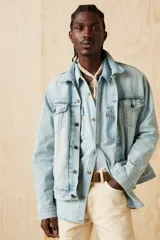 Campera de jean celeste claro, con cuello clásico, cierre frontal con botones metálicos y bolsillos con solapa abotonada en el pecho.