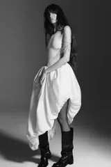 Vestido midi color blanco, de punto fino con cuello redondo y tirantes. Presenta una silueta ajustada en la parte superior y una falda asimétrica con volumen y frunces.