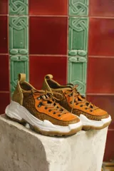 Zapatillas urbanas color óxido, con cordones marrones, suela gruesa blanca y detalles en cuero texturizado.