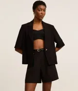 Short color visón de corte sastrero, tiro alto, con pliegues delanteros, trabillas y cinturón fino de cuero sintético.