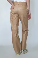 Pantalón de cuero color beige, de corte recto y tiro alto. Presenta bolsillos delanteros y traseros, y trabillas para cinturón.