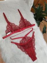 Conjunto de lencería de encaje color rojo, compuesto por un bralette triangular con breteles finos y una tanga con diseño de tiras cruzadas y detalles de encaje.