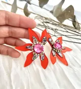 Aros colgantes con forma de flor naranja y centro con gemas rosas y rojas.