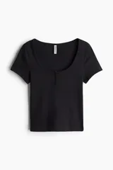Remera corta de punto suave, color negro, con ajuste entallado, escote redondo amplio y tapeta con botones al frente.