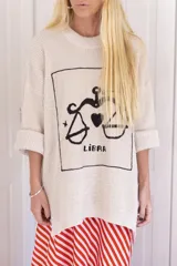 Sweater de punto oversize color crudo, con cuello redondo y diseño bordado a mano en el frente representando al signo Cáncer con un cangrejo, un corazón y una estrella.
