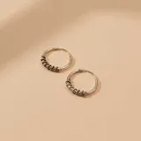 Aros tipo argolla pequeña fabricados en plata 925, con un diseño que presenta una sección texturizada con pequeños relieves decorativos.