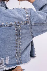 Campera de jean cropped con tachas plateadas distribuidas en el frente, hombros y mangas. Presenta un diseño con bordes deshilachados, cuello clásico y cierre frontal con botones metálicos.
