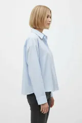 Camisa de algodón a rayas celestes y blancas, de corte holgado, con cuello camisero, cierre frontal de botones y mangas largas con puños rectos.