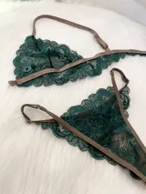 Conjunto de lencería compuesto por un bralette de encaje verde esmeralda con cierre frontal y una tanga a juego con tiras regulables, ambos con detalles de ribetes en color marrón.