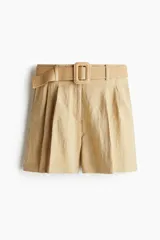 Short de sarga color beige de corte holgado y tiro alto, con pinzas y pliegues delanteros y traseros. Incluye cinturón ancho extraíble con hebilla rectangular decorada y bolsillos laterales y traseros.