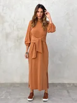 Vestido largo color verde militar, con cuello redondo, mangas largas abullonadas con puños elásticos y detalle de lazo anudado en la cintura. Presenta una abertura lateral en la falda.