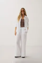 Camisa oversize blanca de manga larga con cuello camisero, bolsillo frontal en el pecho y cierre de botones.