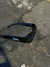Gafas de sol negras con montura rectangular, lentes oscuras y detalle de estrella plateada en el lateral.