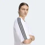 Remera Adidas de corte holgado, color blanco, con cuello redondo y mangas cortas. Presenta las icónicas tres tiras de la marca en color negro a lo largo de las mangas y el logo del Trifolio bordado en el pecho.