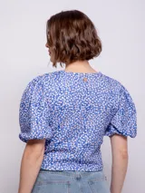 Top corto azul con estampado floral de flores blancas y naranjas. Presenta escote en V con cierre frontal de botones y mangas abullonadas cortas.