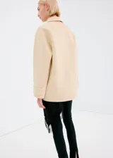 Chaqueta de corte recto color beige, con cuello camisero, cierre frontal de botones oscuros y cuatro bolsillos con solapa en el frente.