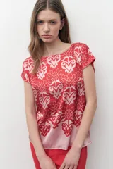 Blusa de satén con estampado floral bicolor en tonos rojo y rosado, de corte recto, cuello redondo y mangas cortas.
