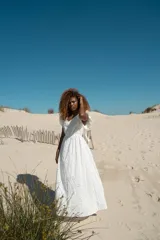 Vestido largo blanco con bordado calado, escote en V, mangas cortas con volados y lazo ajustable en la cintura.