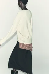 Jersey oversize de punto color crema, con cuello redondo y manga larga. Presenta costuras marcadas en los hombros y los laterales.