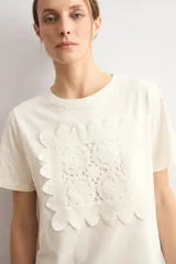 Remera color natural de manga corta, con cuello redondo y un aplique cuadrado de crochet con diseño floral en el centro del pecho.