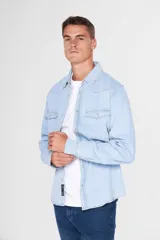 Camisa de jean celeste de manga larga, con cuello clásico, cierre frontal con botones a presión, dos bolsillos con solapa abotonada en el pecho, corte en hombros y detalle en la espalda.