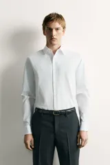 Camisa de corte regular fit color celeste, confeccionada en tejido fácil de planchar. Cuenta con cuello italiano abierto, manga larga con puño abotonado y cierre frontal con botonadura.