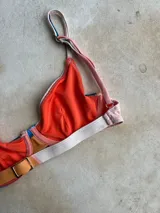 Top de bikini con aro, diseño de bloques de color en tonos azul, naranja y crema, con breteles regulables y cierre metálico en la espalda.