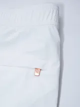 Short de baño blanco con cintura elástica y cordón ajustable. Tiene un parche cuadrado de color beige claro en la pierna izquierda.