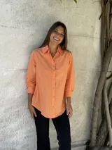 Camisa color salmón con cuello clásico, cierre frontal con botones y mangas largas con puños abotonados.
