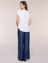 Remera blanca de punto acanalado con escote redondo adornado con tachas metálicas en el cuello y hombros, mangas cortas japonesas y ruedo curvo.