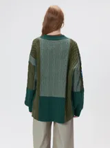 Cardigan oversize de tejido de punto grueso con diseño de bloques de color en tonos tierra. Presenta cuello en V, cierre frontal con botones, mangas largas con terminación abullonada y parches decorativos en el pecho y hombro.