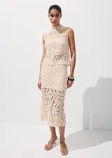 Top de tejido calado color beige, con cuello halter, sin mangas y cierre de botones en la espalda.